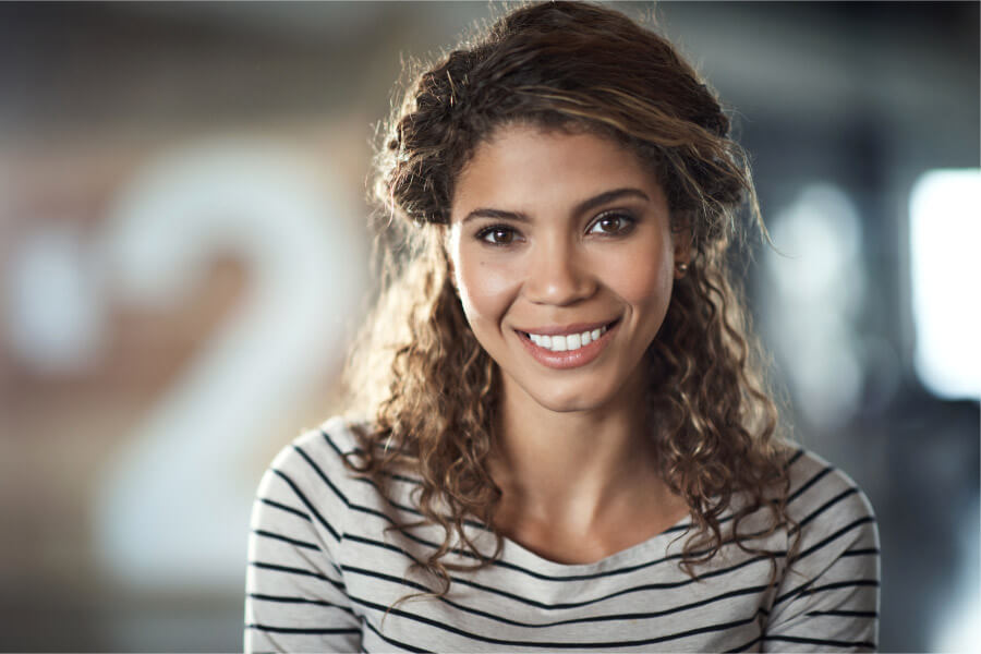 Curly brunette woman with dental implants smiles while wearing a black and white striped shirt