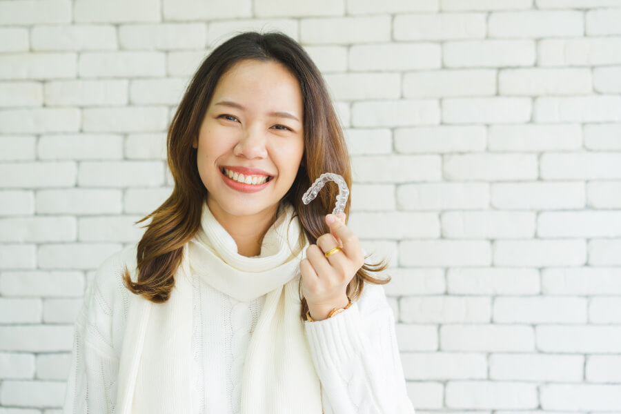Brunette woman smiles as she holds up her Invisalign clear aligners in Gastonia, NC