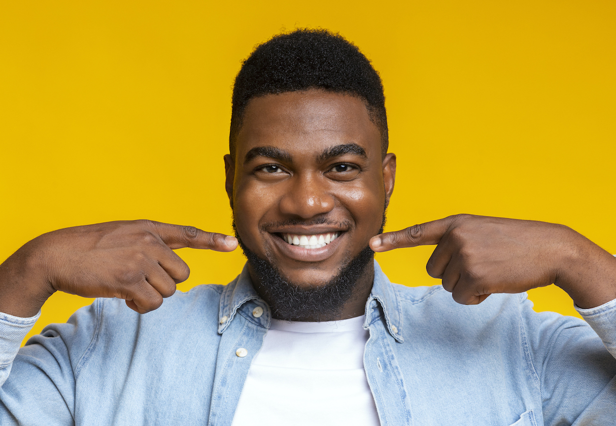 Black man smiles and points to his teeth in front of a yellow background