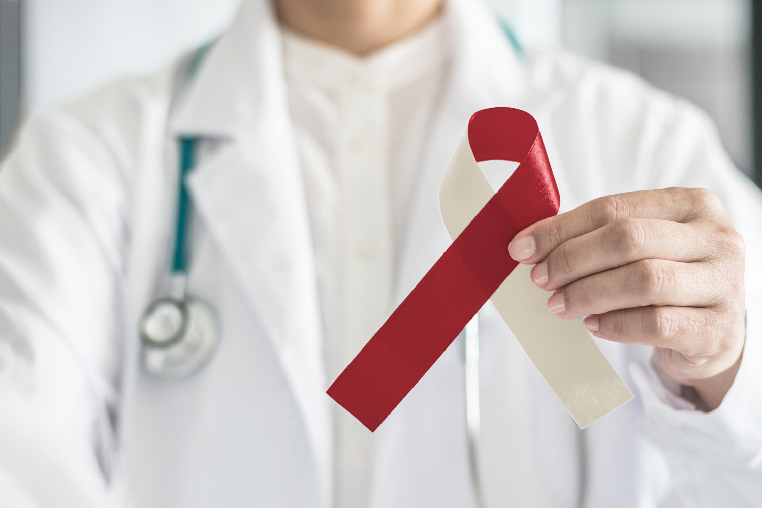 Closeup of a dentist in a white lab coat holding a red and beige ribbon for Oral Cancer Awareness Month